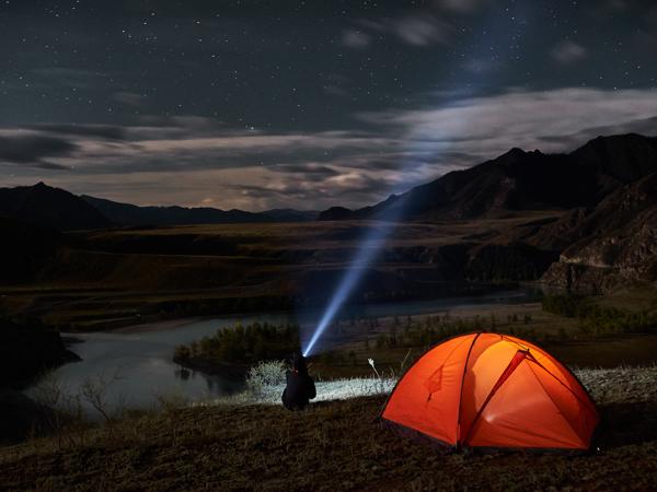 Man using flashlight in campsite at night